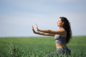 Woman meditating in a large, grassy field