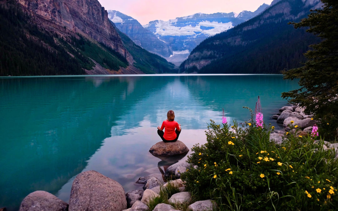 Woman in seated meditation on a rock overlooking beautiful blue waters and mountains