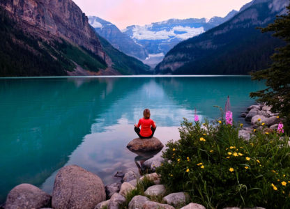 Woman in seated meditation on a rock overlooking beautiful blue waters and mountains