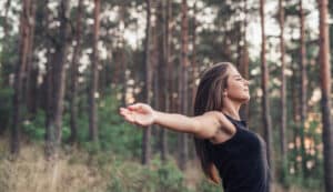 woman with arms open in the forest practicing qigong